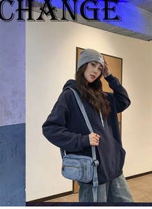 Detail of vintage washed denim crossbody bag with multiple zipper pockets on a hoodie