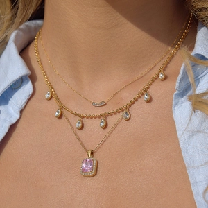 Detail of layered gold necklaces featuring a large pink rectangular gemstone pendant
