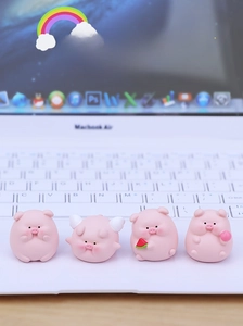 Set of four cute mini pink resin pig figurines displayed on a laptop keyboard