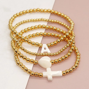Detail of four-piece gold beaded bracelet set with heart, cross, and letter A charms