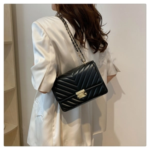 Detail view of the black V-quilted crossbody bag with gold lock and chain strap on model