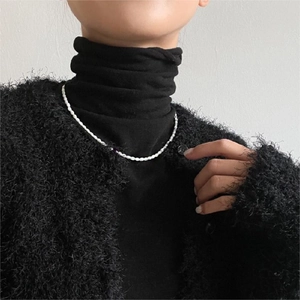 Detail of white beaded pearl necklace worn over a black turtleneck for a contrast look
