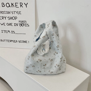 Detail of light blue floral canvas handbag with delicate white lace trim and knot handle
