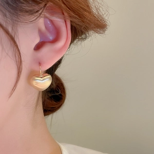 Close-up of golden brushed heart earrings with hooks on a female model for fashion