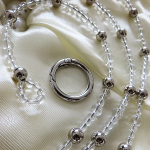 Catena per borsa con perle trasparenti e argento su sfondo di seta color champagne