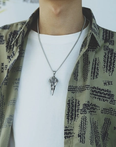 Macro detail of a vintage silver crow skull pendant on a stainless steel chain for men