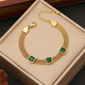 Gold mesh chain bracelet with three square green gemstones on a beige jewelry box