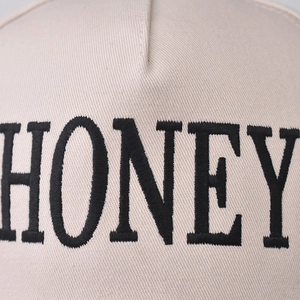 Beige cotton baseball cap with black HONEY embroidery detail and premium stitched texture