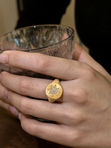 Detail of gold-plated signet ring with starburst pattern and small crystals on finger
