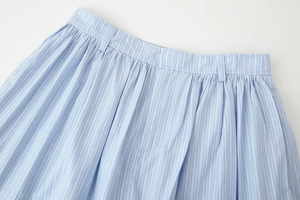 Detail of light blue striped skirt waist with fine pleats and belt loops on white background