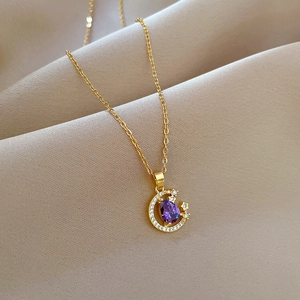 Macro detail of crescent moon necklace with purple pear-shaped gem on beige fabric