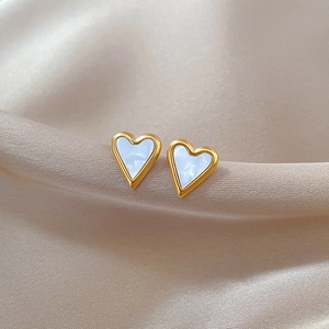 Macro shot of heart-shaped titanium steel earrings with white shell inlay on silk fabric