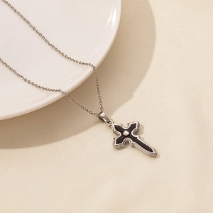 Macro shot of gothic silver and black cross pendant necklace on white ceramic plate