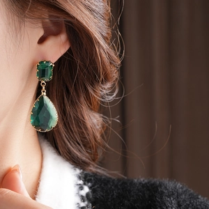 Dettaglio di modella che indossa orecchini a goccia stile smeraldo con finiture oro