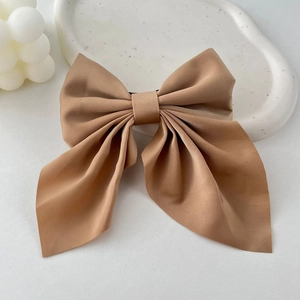 Detail of light brown fabric bow hair clip on a white decorative ceramic plate