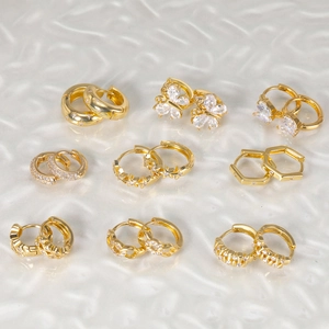 Detail showing nine pairs of gold butterfly and star zircon huggie earrings on wavy base