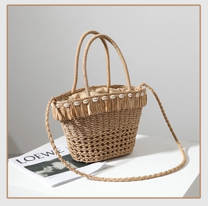 Dettaglio borsa in paglia intrecciata con decorazioni di conchiglie e nappe in rafia