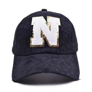 Detail of sequined N letter patch and distressed cotton texture on black baseball cap