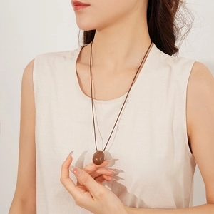 Détail d'un collier pendentif ovale marron avec cordon ciré porté sur un mannequin en beige