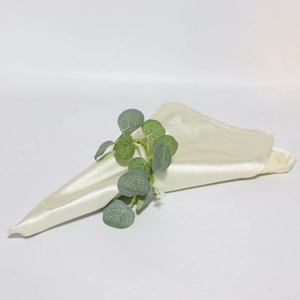 Macro shot of cream beige satin napkin with artificial eucalyptus leaf decoration