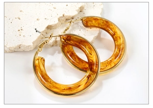 Detailed close-up of golden metal earrings with amber resin hoop on travertine stone