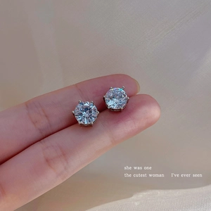 Detail view of silver zircon stud earrings with six-claw setting on soft fabric background
