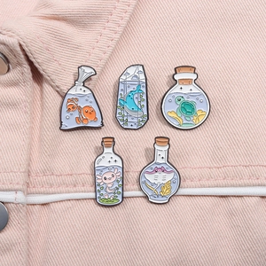 Macro shot of 5 cartoon ocean animal enamel pins in bottles on pink denim fabric