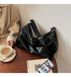 Détail du sac cabas en cuir noir brillant avec boucle argentée sur table en bois