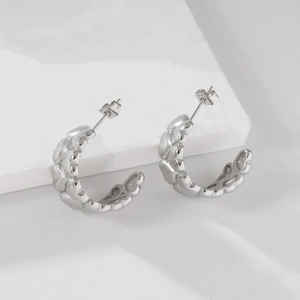 Polished silver heart textured hoop earrings on white minimalist stone background