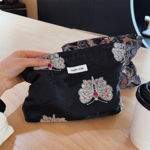 Detail of black satin cosmetic bag with floral embroidery and Simple Wish logo tag