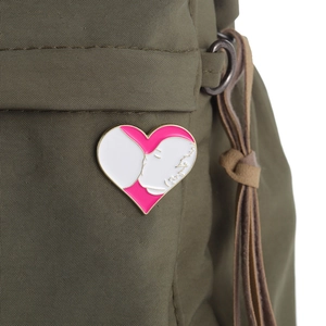 Detail of pink and white heart enamel pin on a green canvas bag showing maternal art