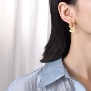 Close-up of a minimalist golden crescent moon earring worn on a female model's ear