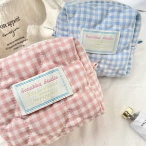 Quilted plaid makeup organizer bags in pink and blue colors on soft white fabric