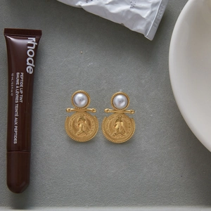 Detailed view of vintage gold coin earrings with pearl accents on a textured desk