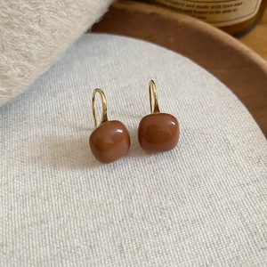 Macro view of caramel tiger eye C-shape square earrings on white textured fabric