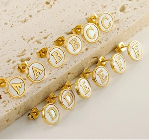 Close-up of gold-plated titanium steel round alphabet earrings with shell inlay