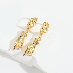 Detail of gold palm pendant earrings with purple nails and sparkling eye motif