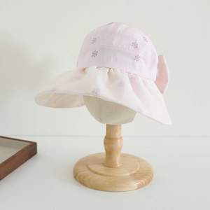 Close-up of pink sun hat featuring floral prints and a large bow on a wooden stand