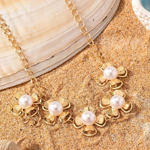 Elegant gold flower necklace with white pearls displayed on a beach seashell