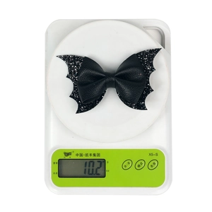 Detail showing a black glitter bat bow hair clip weighing 10.2g on a scale
