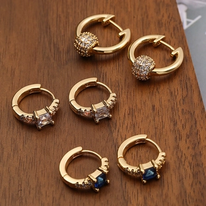 Three gold plated geometric hoop earrings with zircon and blue gemstones on wood