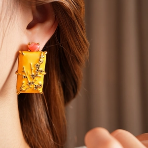 Détail d'une boucle d'oreille vintage carrée en émail jaune avec perle rose et relief floral