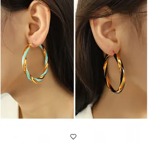 Close-up of chunky gold-plated twisted hoop earrings with sky blue and black enamel details