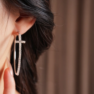 Dettaglio di orecchini a cerchio in argento con ciondolo a croce di strass su modella