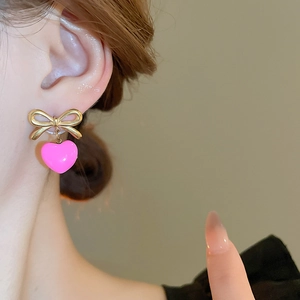 Gros plan sur des boucles d'oreilles nœud doré et cœur rose brillant sur l'oreille