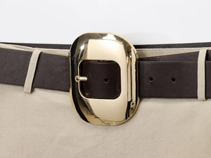 Detail shot of a dark brown belt with a gold oval buckle on a beige midi skirt