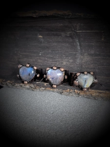 Three vintage heart-shaped labradorite rings with bronze finish on a rustic wood base