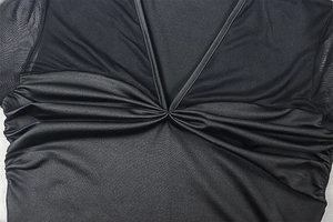 Close-up of V-neckline featuring ruched mesh fabric and sleek knit textures on a black dress