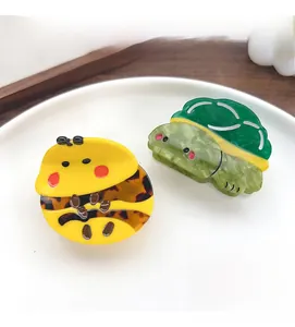 Detail of yellow bee and green turtle cellulose acetate hair claws on a white tray