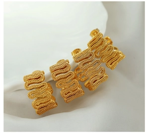 Macro detail of gold S-shaped earrings featuring a dense micro-bead textured surface